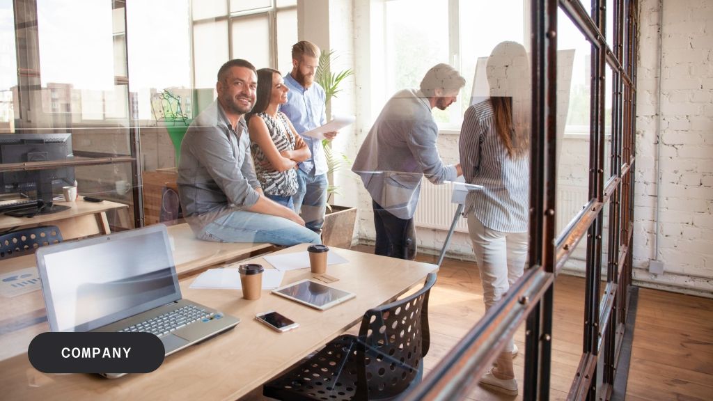 A group of diverse professionals collaborating in a modern office, with one man smiling at the camera.