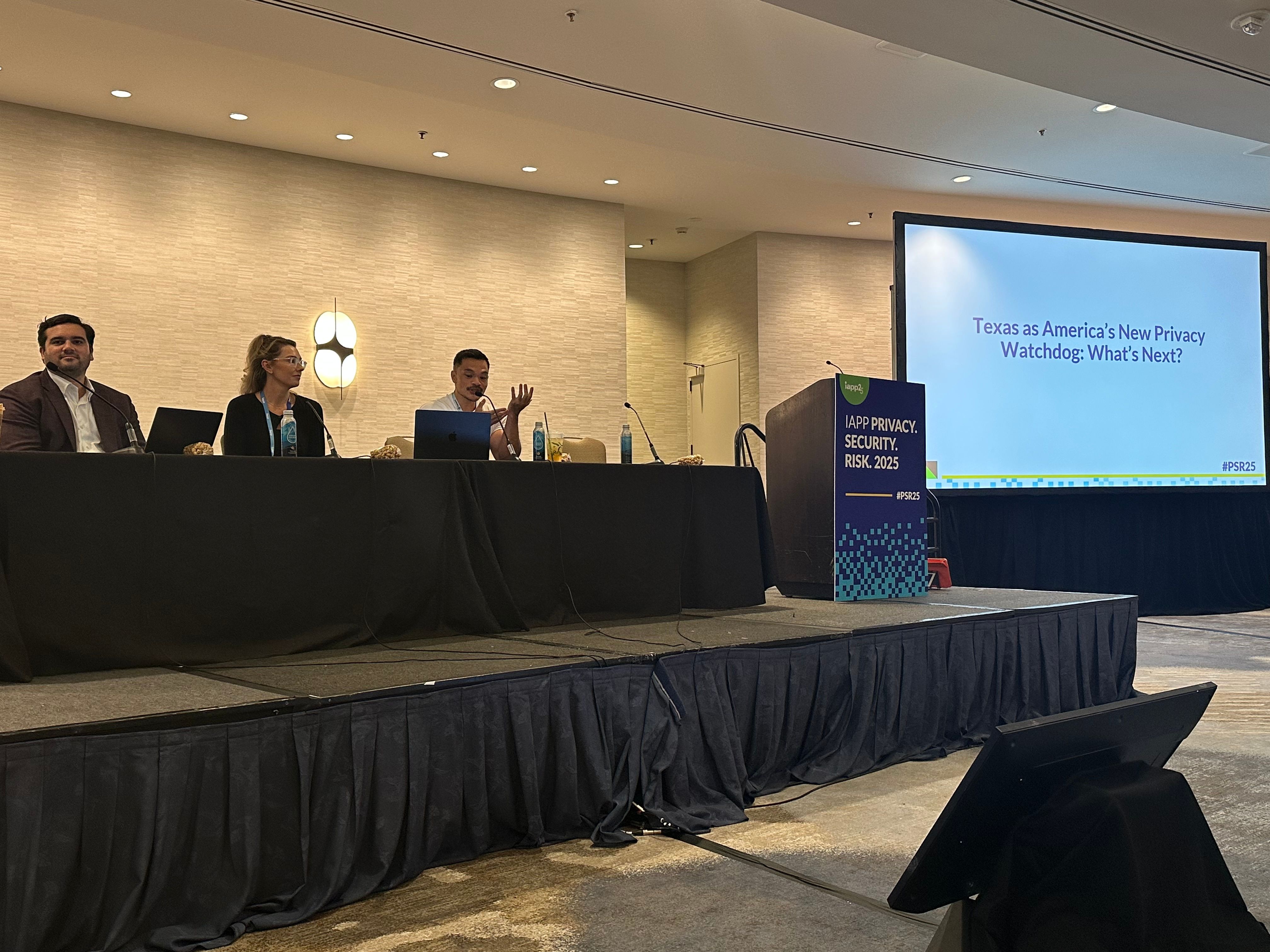 Three people are seated at a panel discussion table on a stage, with a presentation slide in the background reading "Texas as America’s New Privacy Watchdog: What’s Next?"