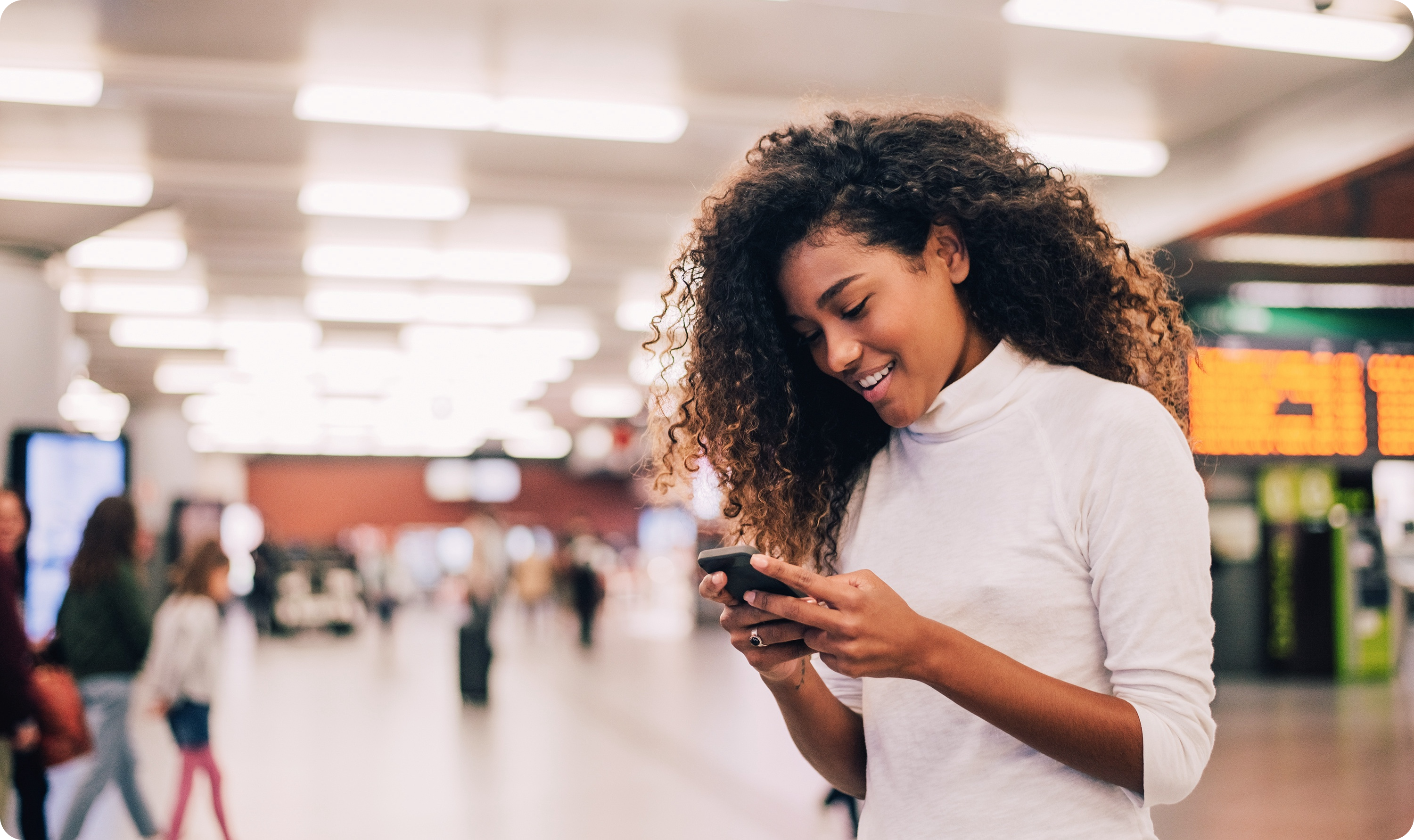 Young women standing in a train terminal smiling while she looks at her phone