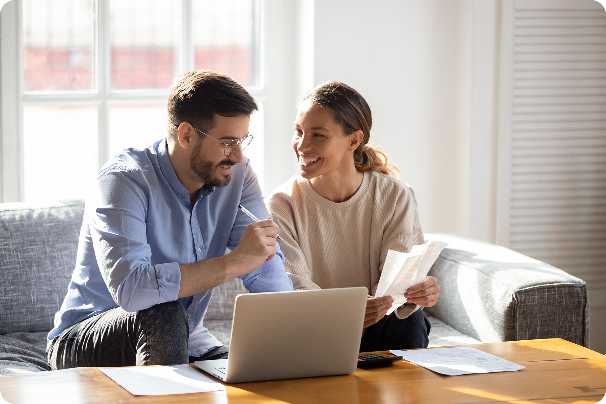 Young couple smiling while doing paper work and looking at a laptop