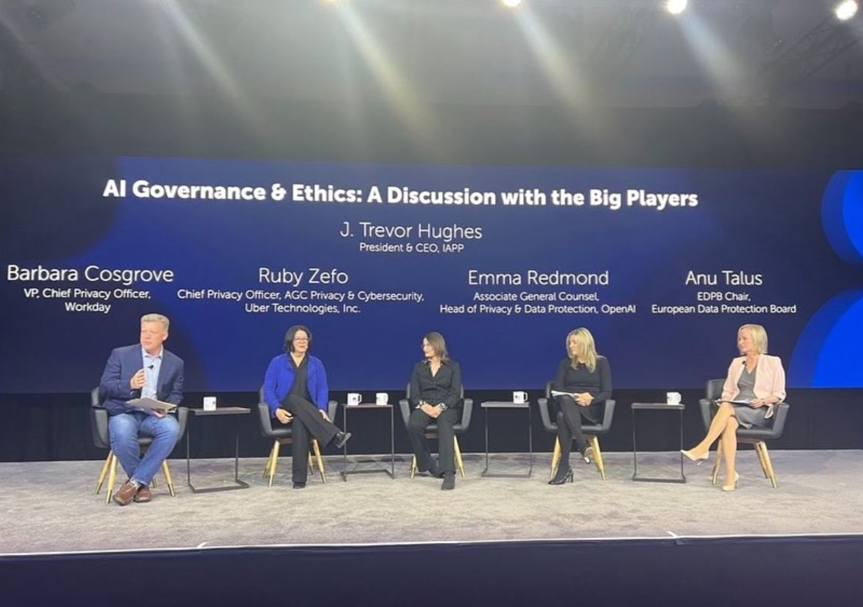 An onstage panel of executives in front of screen displaying their names and the topic: AI Governance & Ethics
