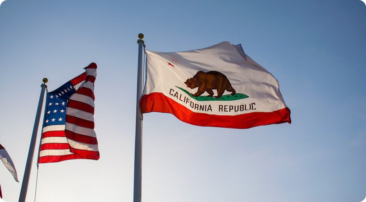 The USA flag and California flag waving in front of blue sky