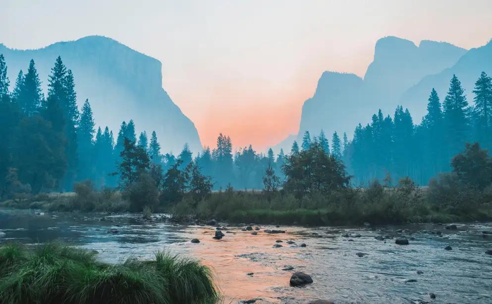 Scenic landscape of river backed by forest and mountains ahead of sunset