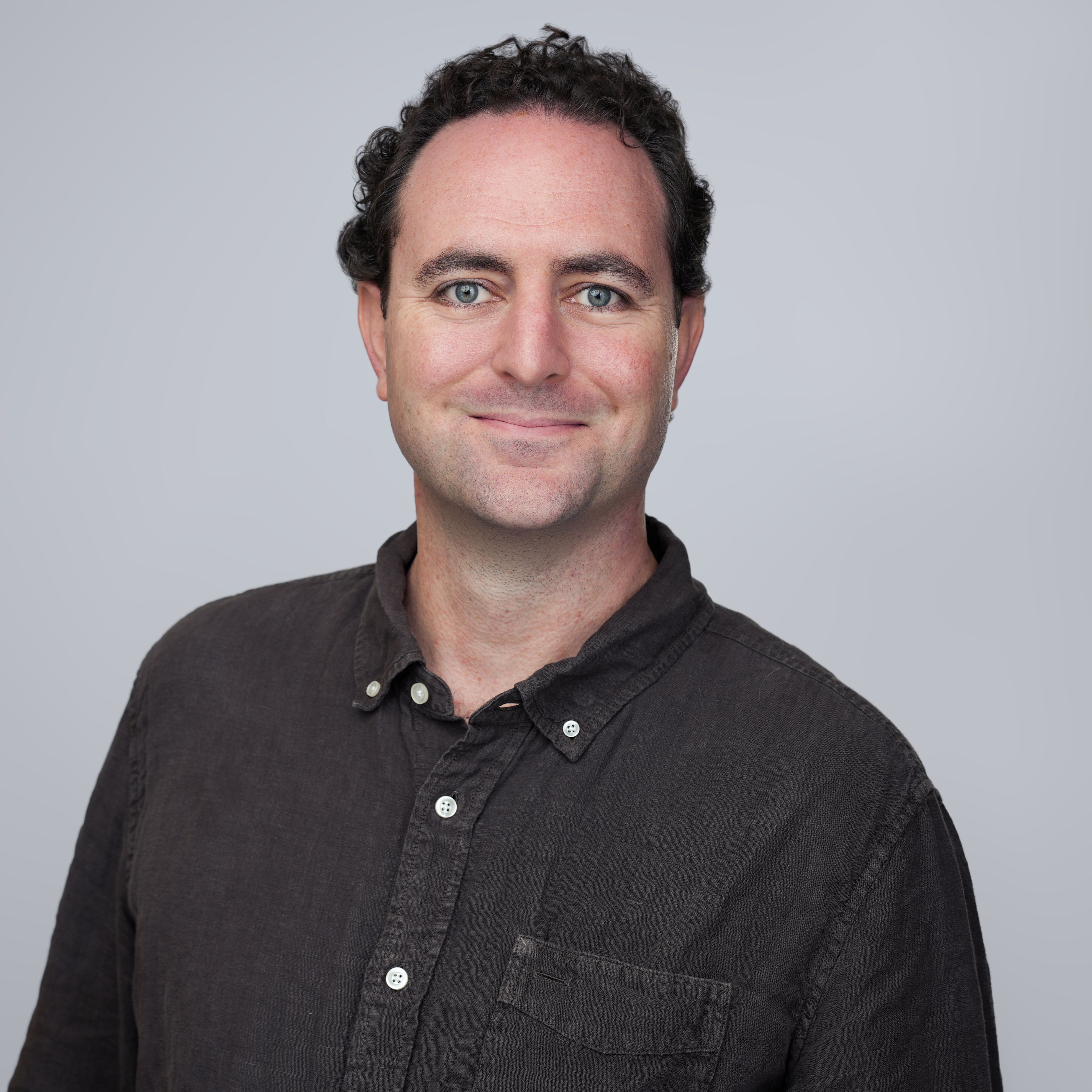 Smiling man with dark curly hair, blue eyes, and a dark shirt.
