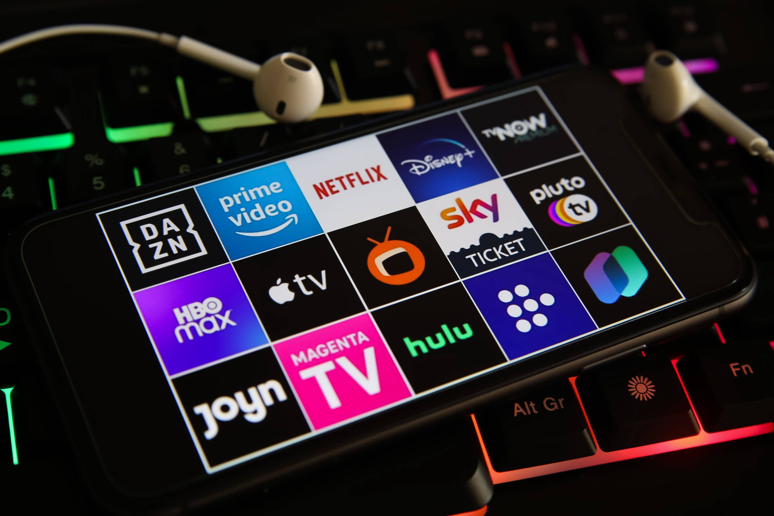 Smartphone laying on an RGB keyboard with various streaming service apps on display