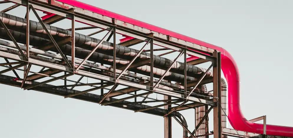 Industrial structure with metal framework supporting black and pink pipes against a clear sky.