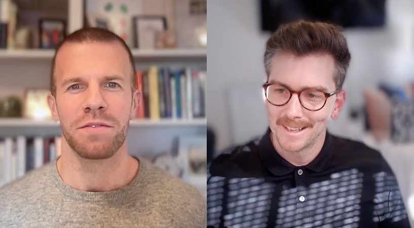 Two men are speaking during a video call; the man on the left has a beard and is in front of a bookshelf, while the man on the right wears glasses and is in a room with blurred background details.