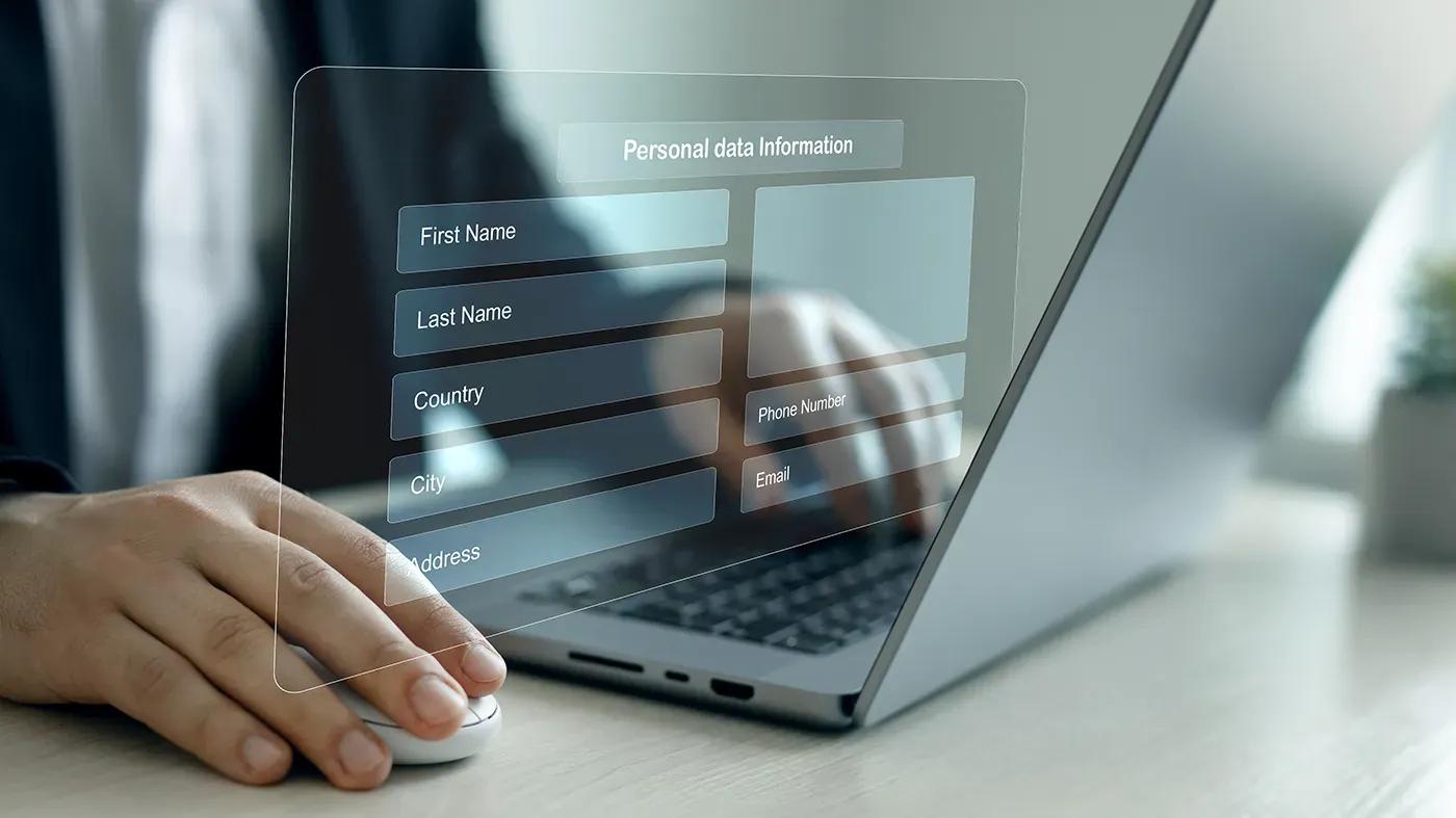 A person uses a laptop with a transparent screen displaying a form for personal data information, including fields for first name, last name, country, city, address, phone number, and email.