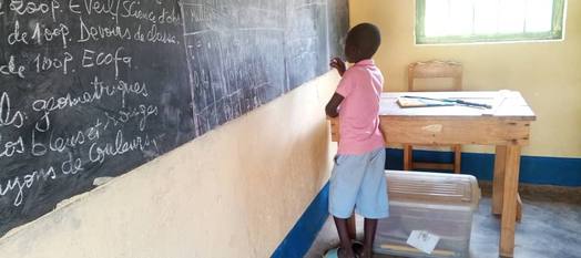 Un élève écrit au tableau noir dans une salle de classe.