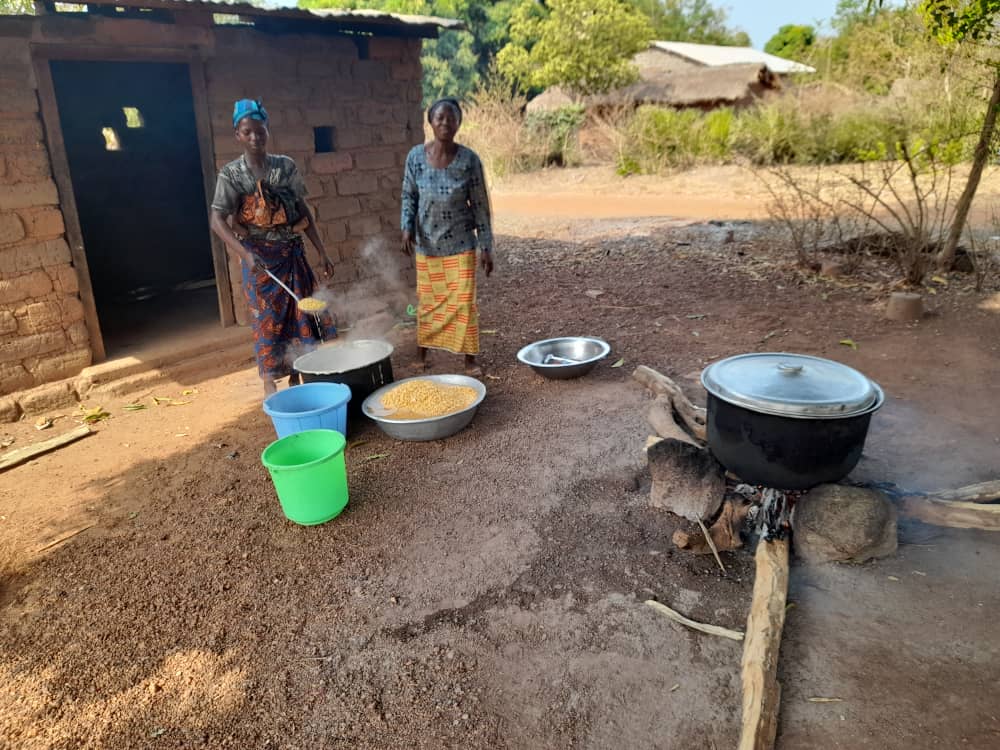 Les cuisinières préparent le repas sur un feu de bois, devant la cuisine.