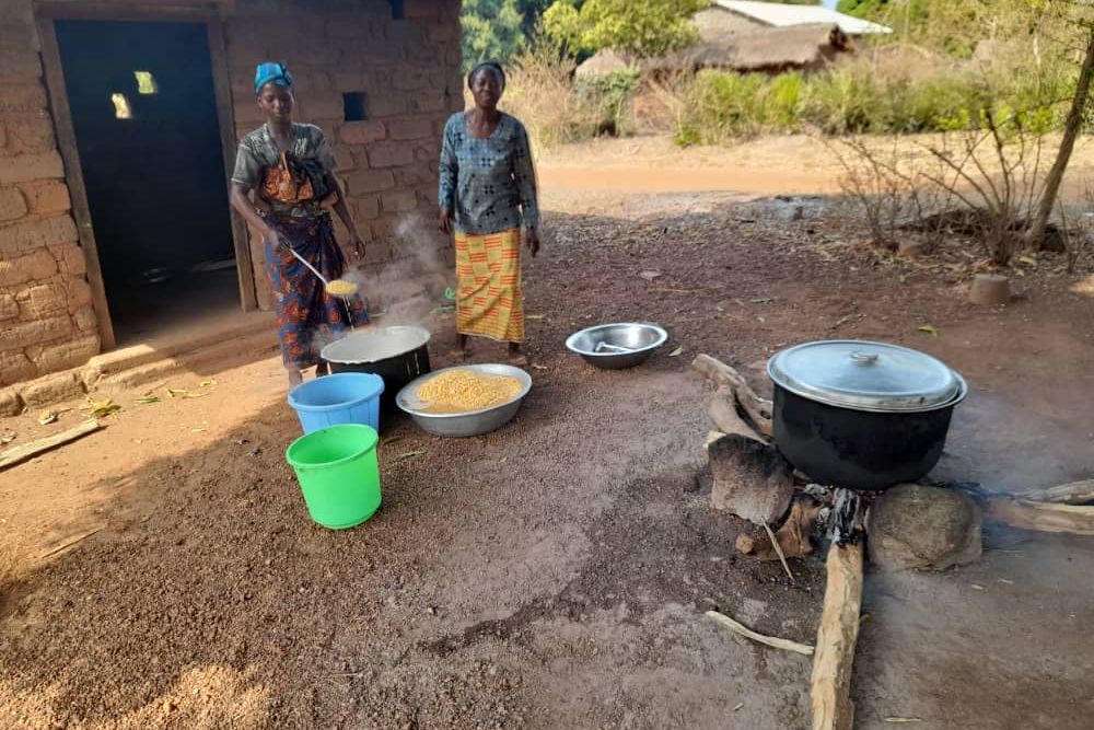 Les cuisinières préparent le repas sur un feu de bois, devant la cuisine.
