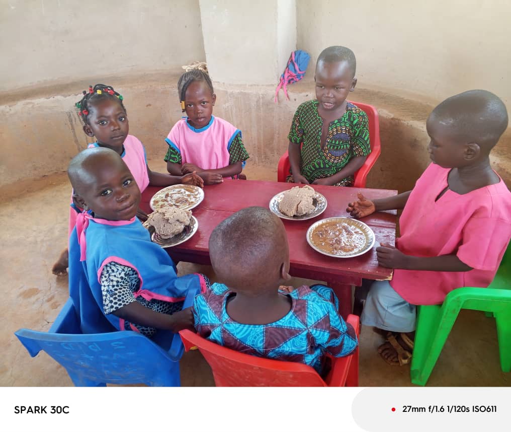 Six jeunes élèves partagent leur repas autour d’une table rouge.