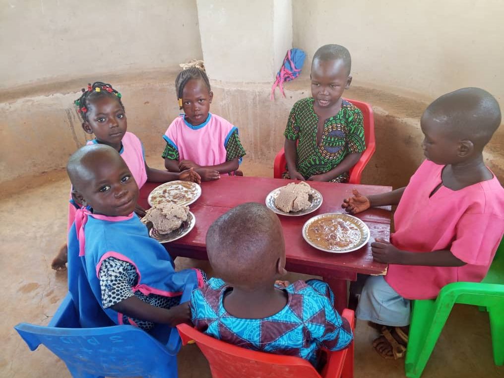 Six jeunes élèves partagent leur repas autour d’une table rouge.
