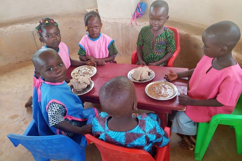 Six jeunes élèves partagent leur repas autour d’une table rouge.