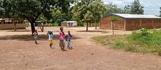 Des élèves traversent la grande cour de l’école, entre les arbres et les bâtiments.