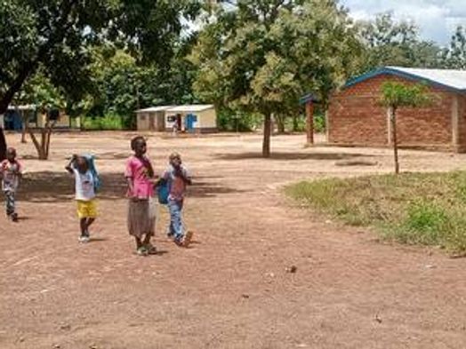 Des élèves traversent la grande cour de l’école, entre les arbres et les bâtiments.