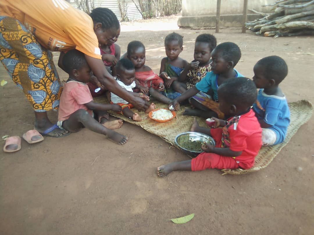 Des enfants assis sur une natte partagent un plat de riz.