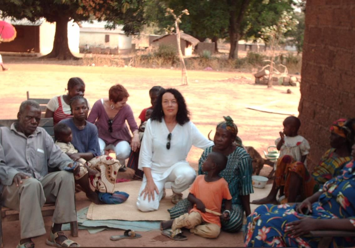 Catherine Parisel, vêtue de blanc, assise sur une natte parmi des enfants et des familles centrafricaines.