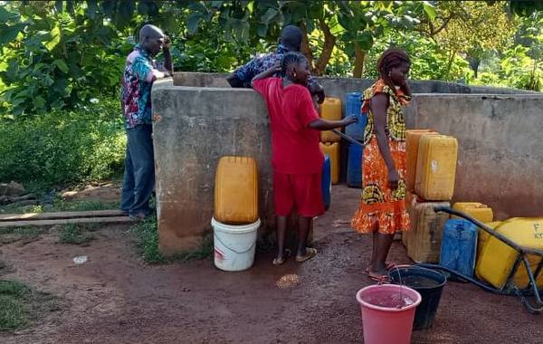 Des habitants remplissent des bidons jaunes au forage de l’école.