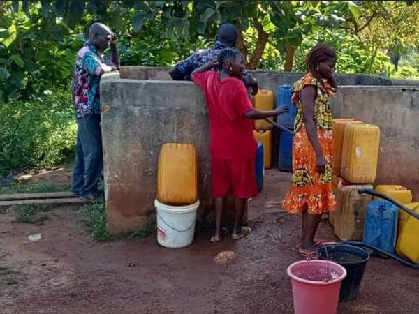 Des habitants remplissent des bidons jaunes au forage de l’école.