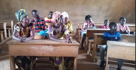 Les tuteurs des cinq enfants réunis dans une salle de classe, assis aux pupitres.