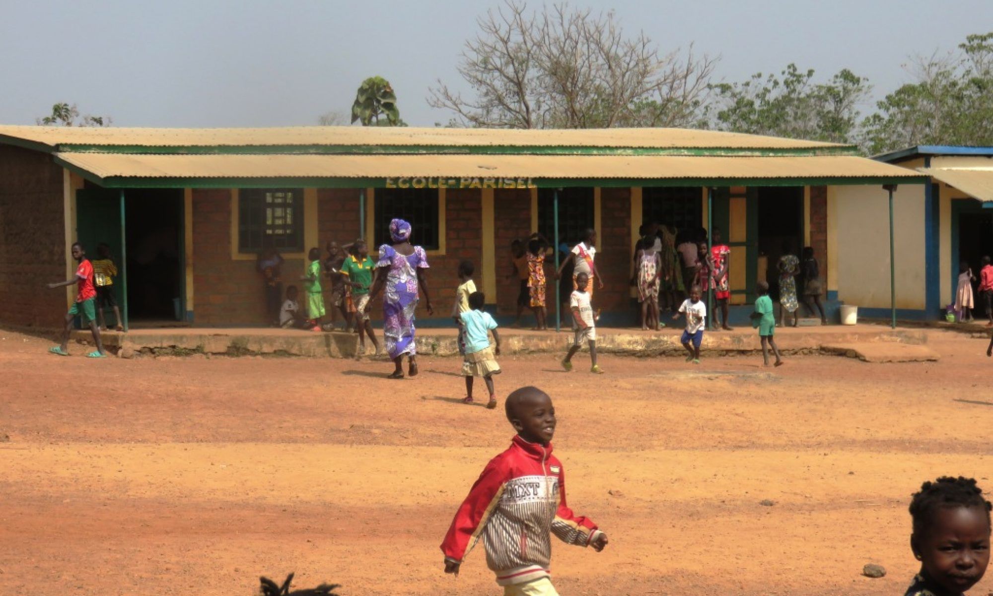 Des enfants courent dans la cour de terre rouge, devant le bâtiment de l’école Parisel.