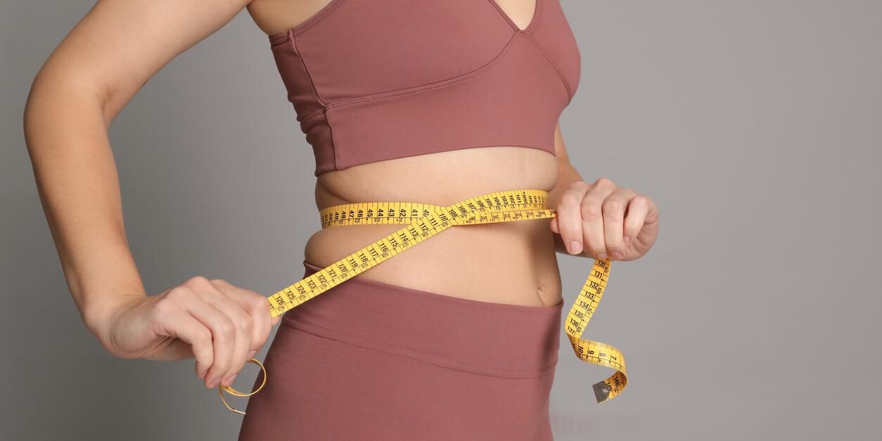 woman holding a measuring tape around her abdomen