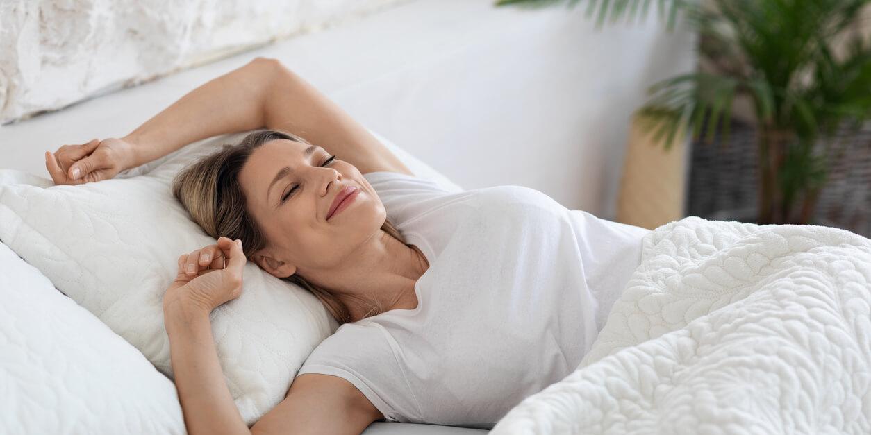 woman smiling while laying in bed with arms up
