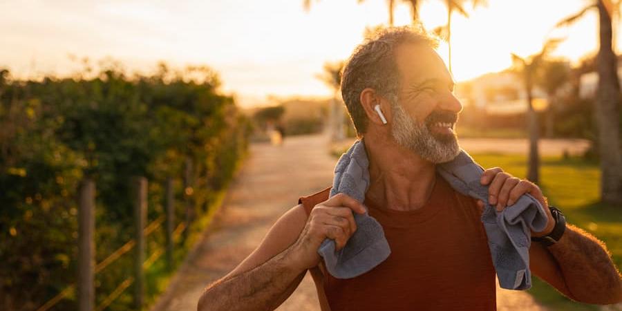 older man smiling while jogging and holding his towel which is around his neck