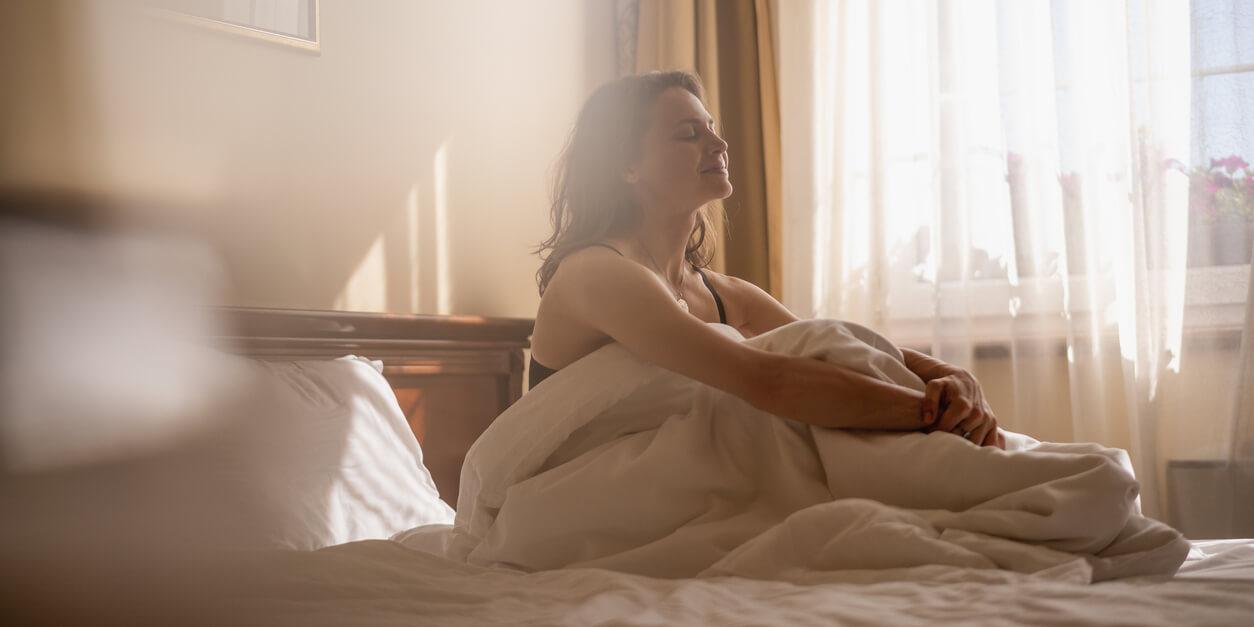 woman sitting in bed smiling holding her knees over sheets