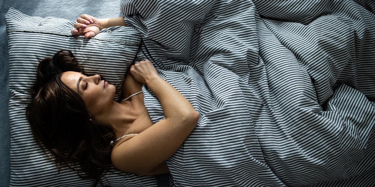 woman sleeping covered with sheets while holdinga pillow