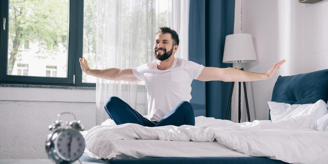 man smiling sitting on the bed stretching his hands