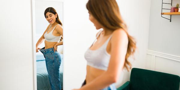woman looking herself in the mirror while holding oversized pants