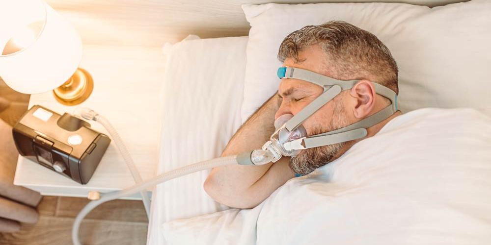 white middle aged man with sleep apnea sleeping with CPAP machine on his face