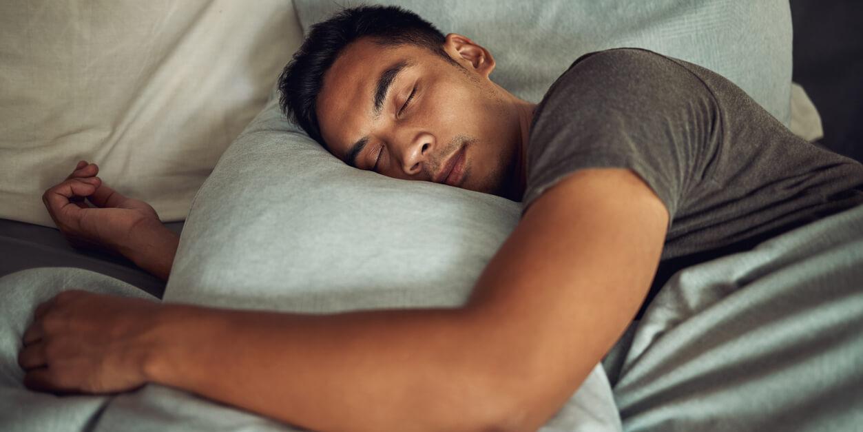 man sleeping while holding a pillow with one hand on top of the pillow