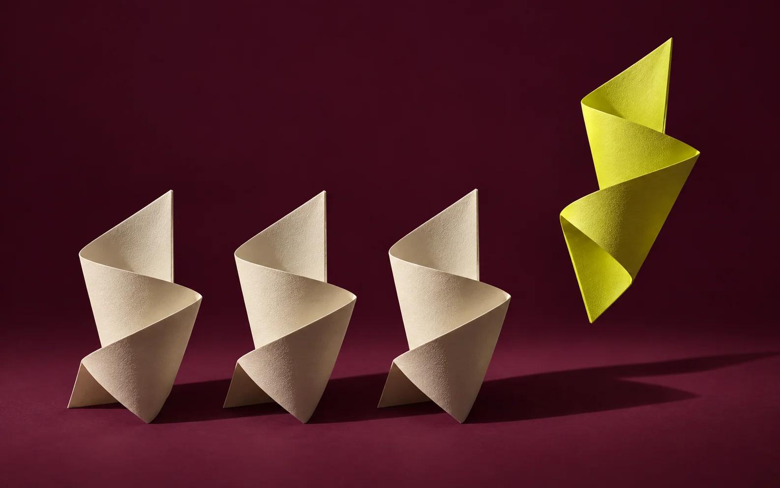 One yellow folded paper sculpture breaks away from identical cream sculptures.