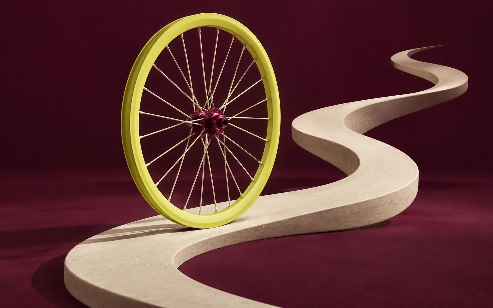 A yellow bicycle wheel stands on a winding cream ribbon road.