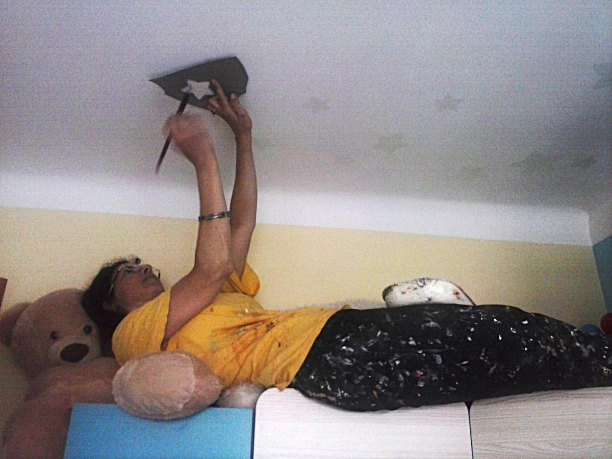 An artist, Joanna Kruza, is laying in the wardrobe with teaddy bear (a toy) under her head and painting stars on the . Private apartment in Warsaw.
