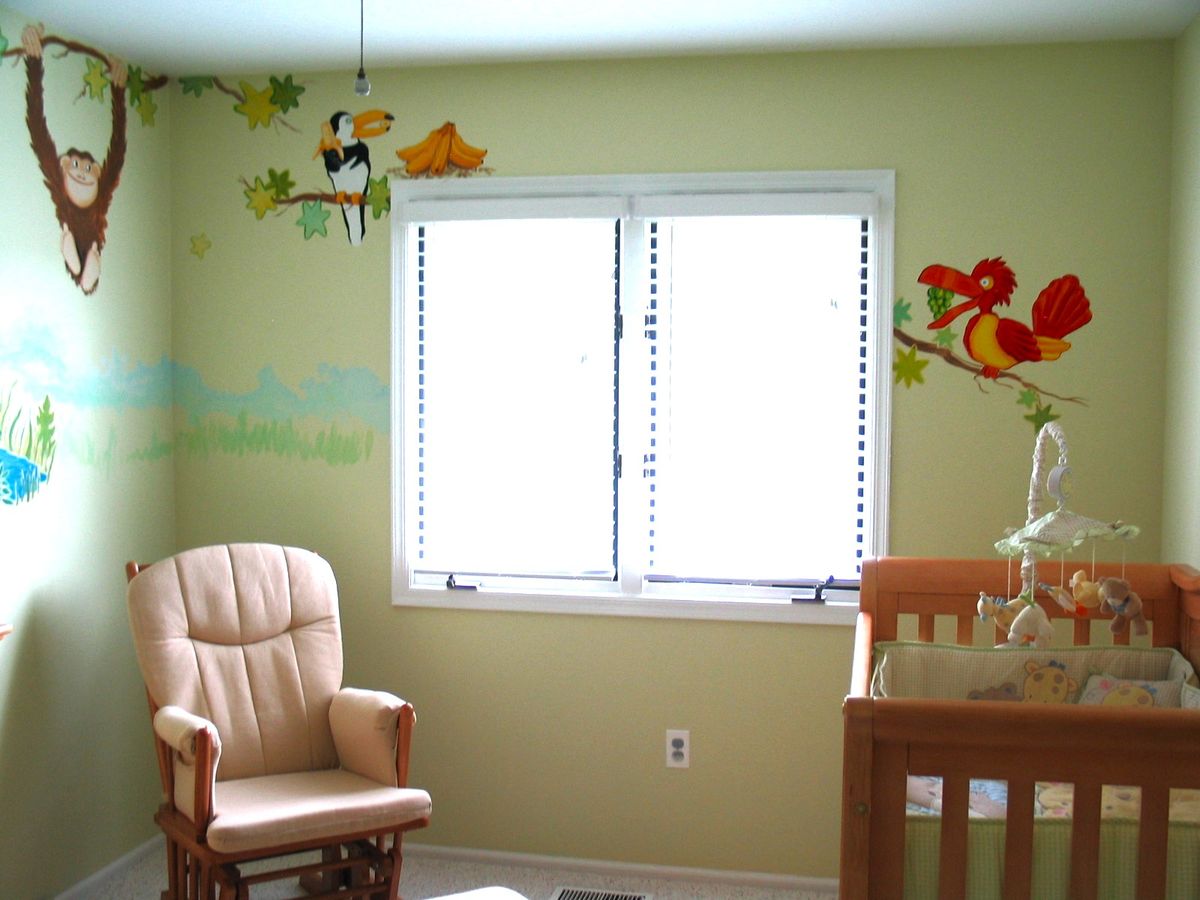 Jungle-themed nursery mural with monkey, toucan, bird and tropical foliage around a cot