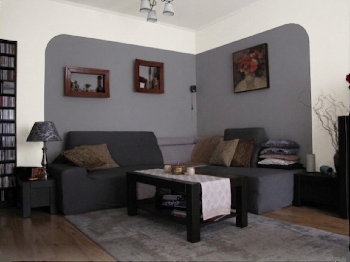 A living room with a sectional sofa and a coffee table, featuring a repainted corner wall with a defined gray color zone.