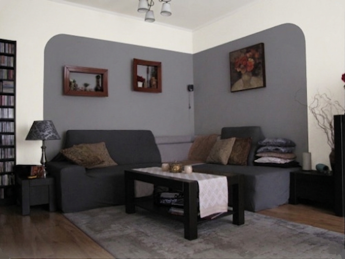 A living room with a sectional sofa and a coffee table, featuring a repainted corner wall with a defined gray color zone.