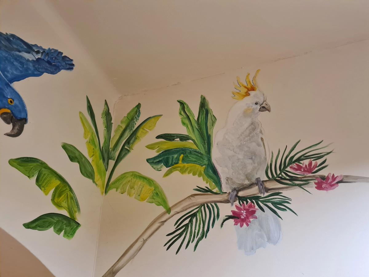Mural tropikalny wkomponowany w narożnik pokoju — biała kakadu  wśród dżungli. Realizacja autorska.