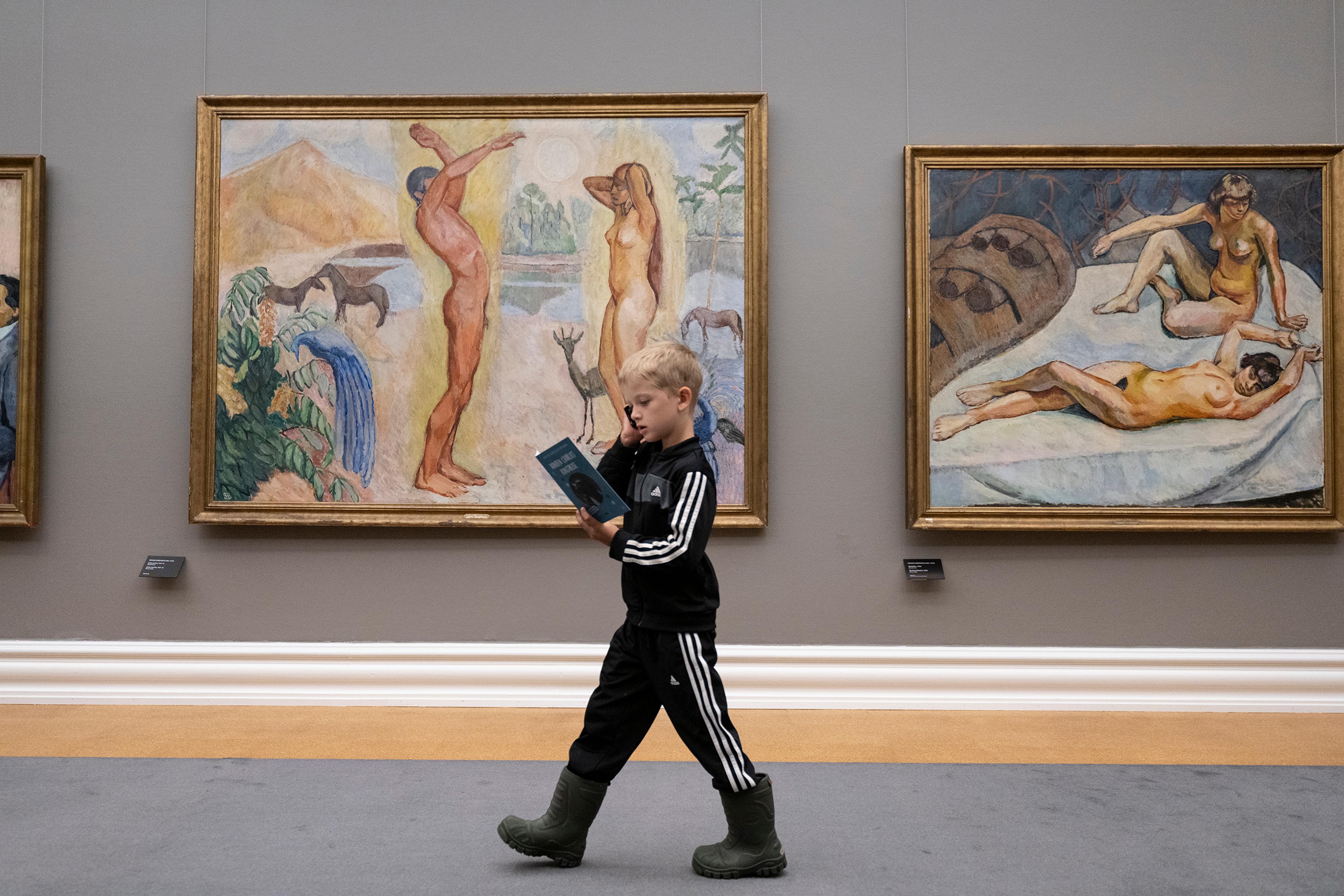 A boy is walking in front of a large painting, listening to an audio guide