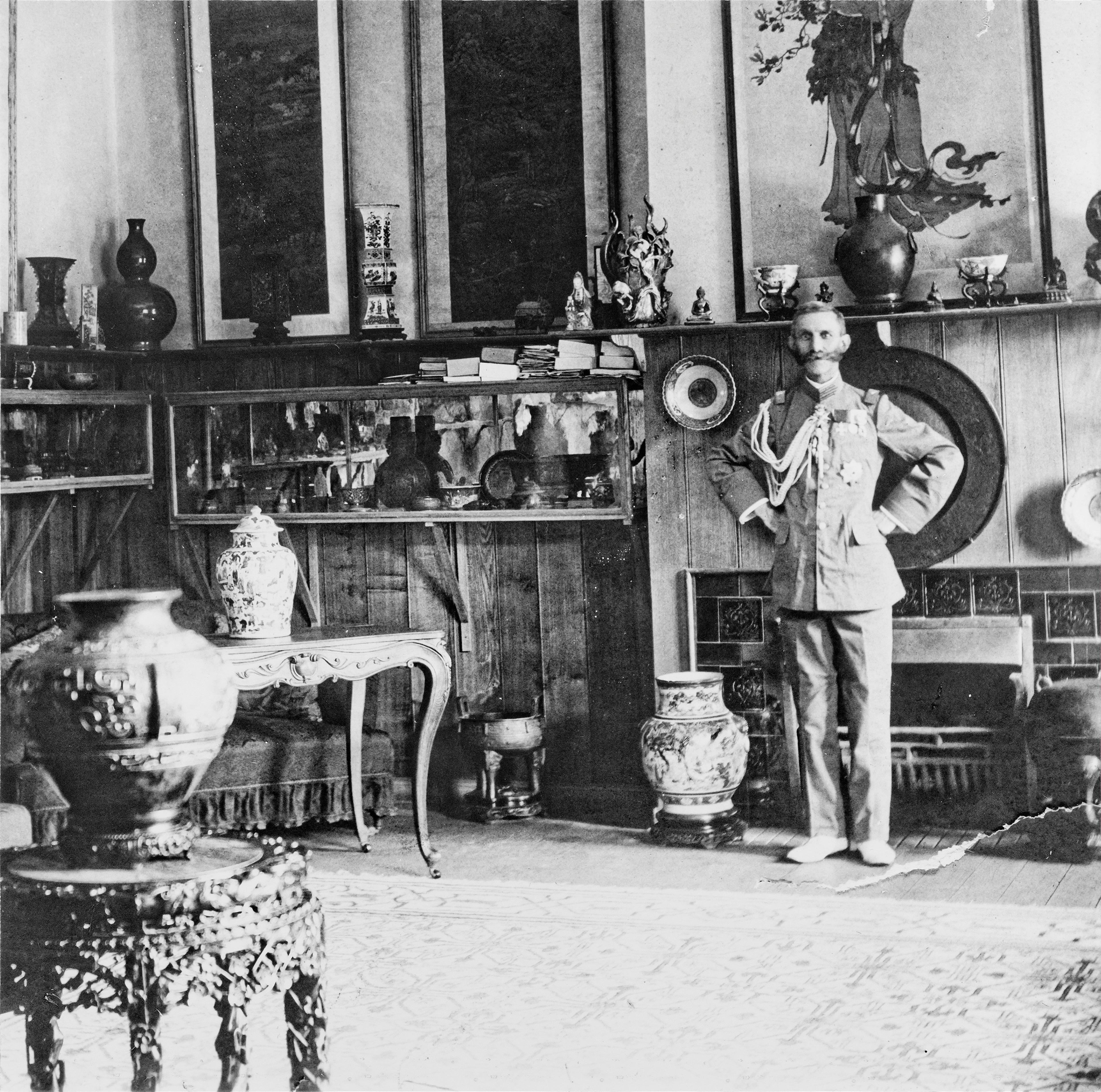 Sort-hvitt foto av general Munthe, som står i et rom i hjemmet sitt i Beijing, omgitt av kinesiske gjenstander og møbler