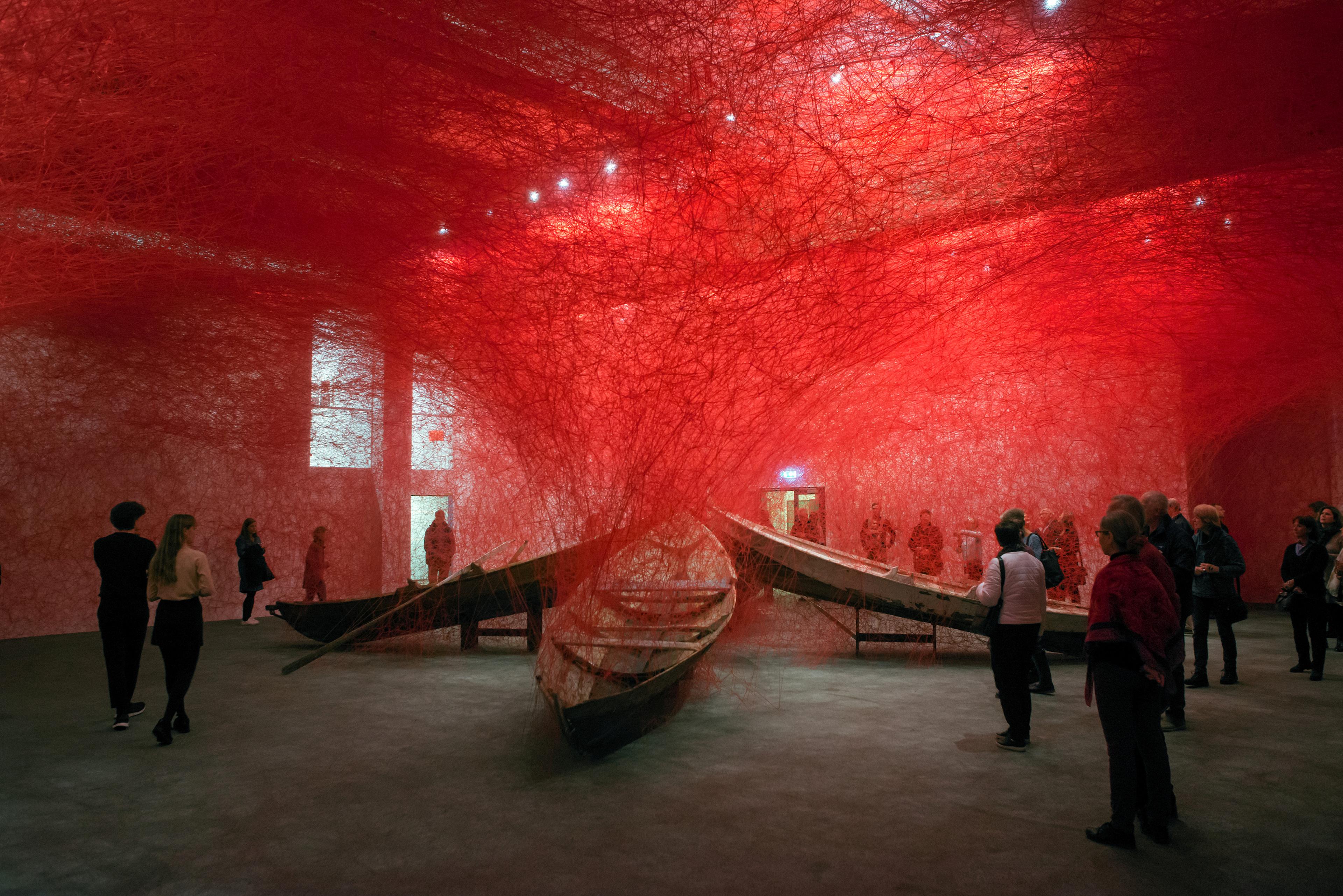 En stor installasjon i museet Stenersen, som viser tre trebåter delvis viklet inn i et nett av røde tråder.