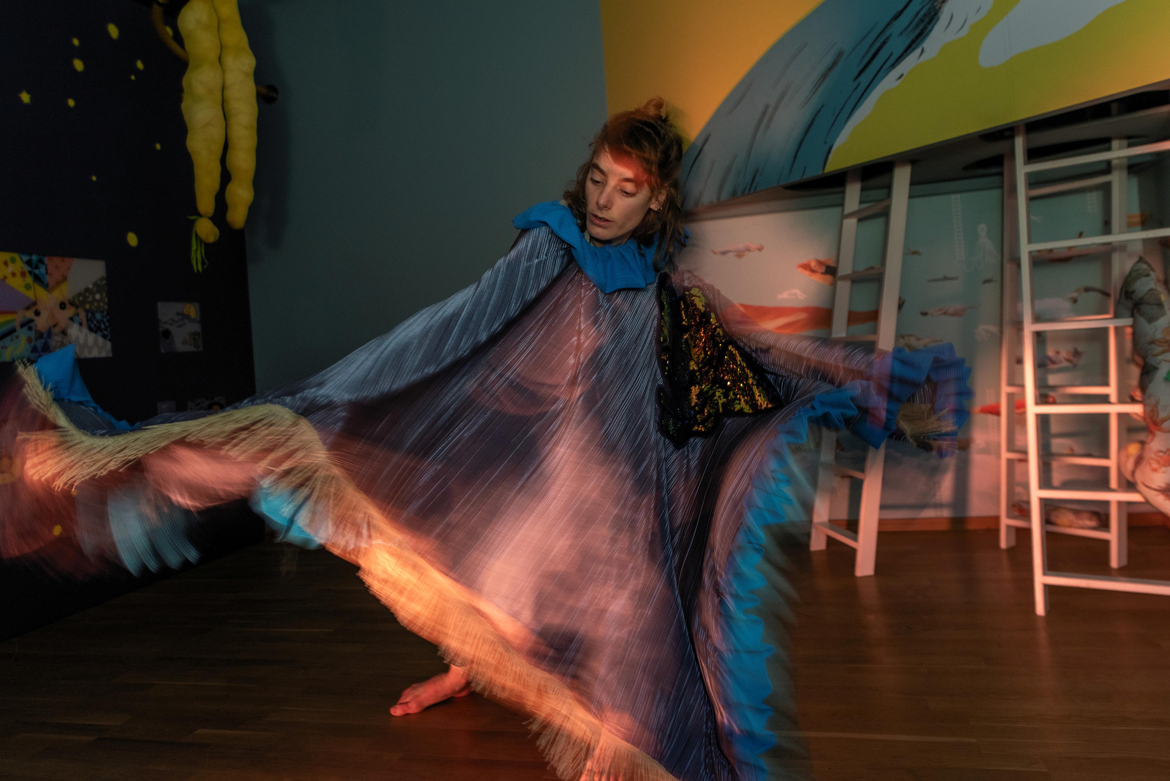 A woman dancing and performing in a colorful dress, in an exhibition for children