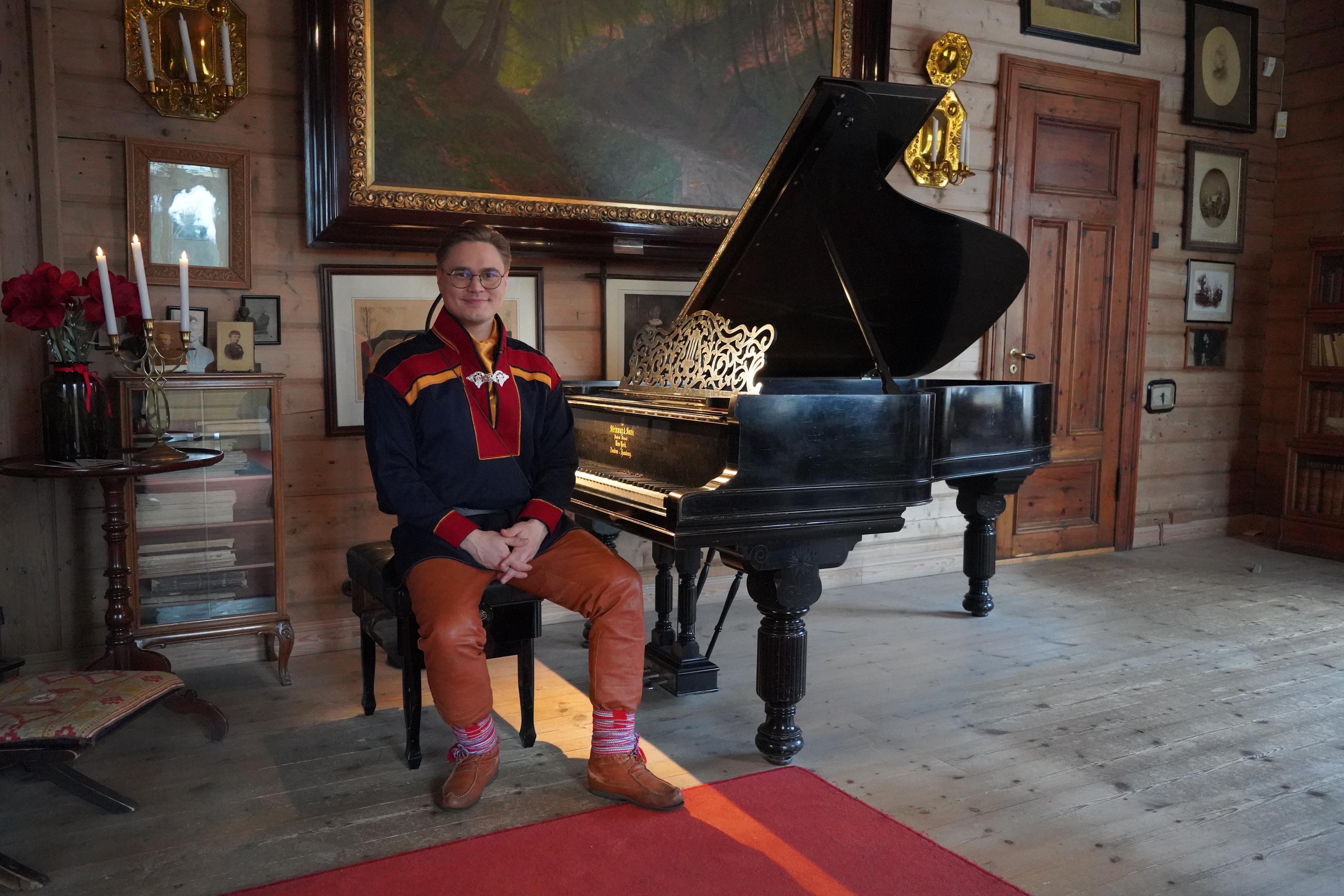 En ung mann i samisk drakt sitter ved Edvard Griegs klaver i stuen på Troldhaugen
