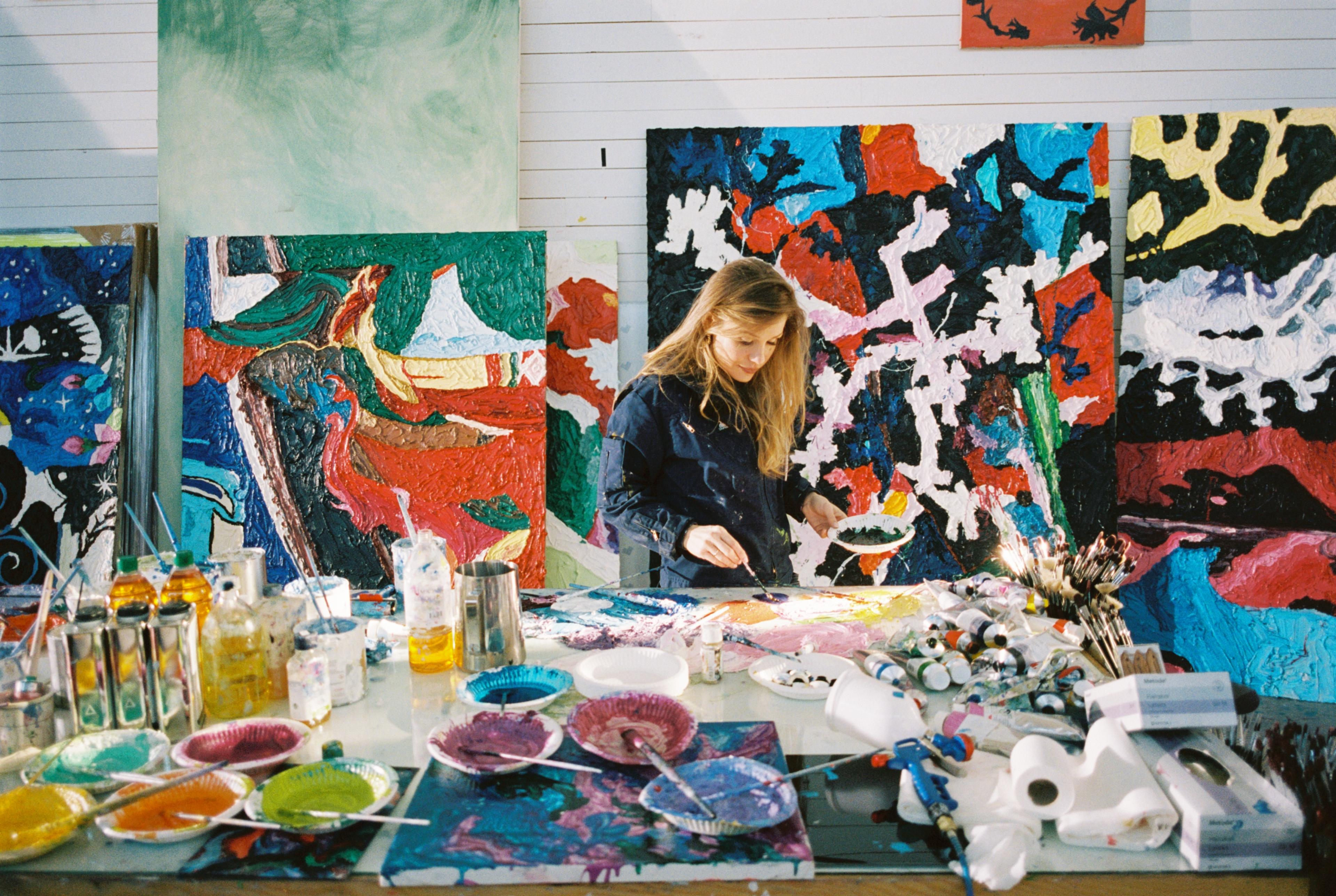 En kvinne står og maler i et atelier.