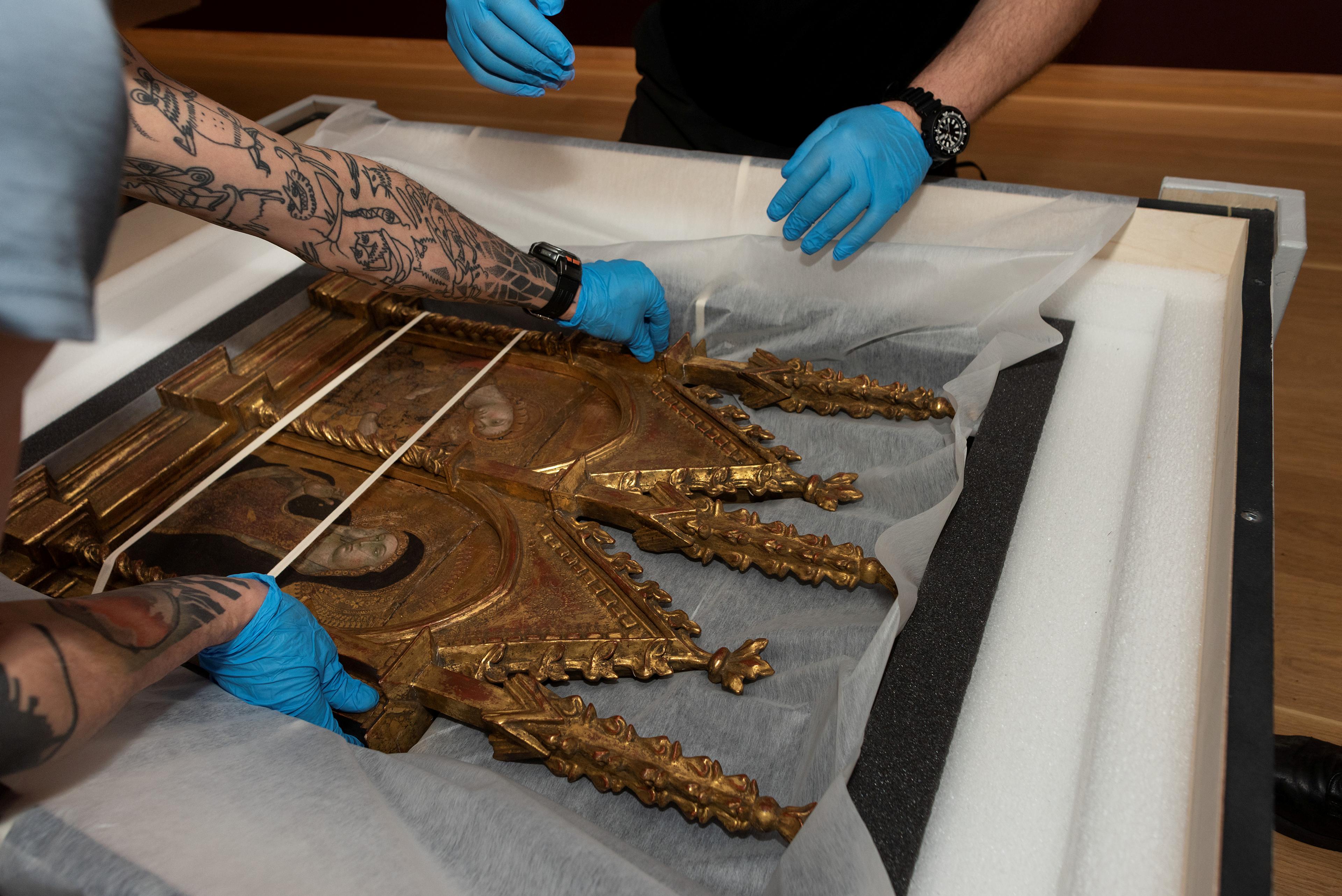 We see two pairs of hands carefully preparing a work for transport.