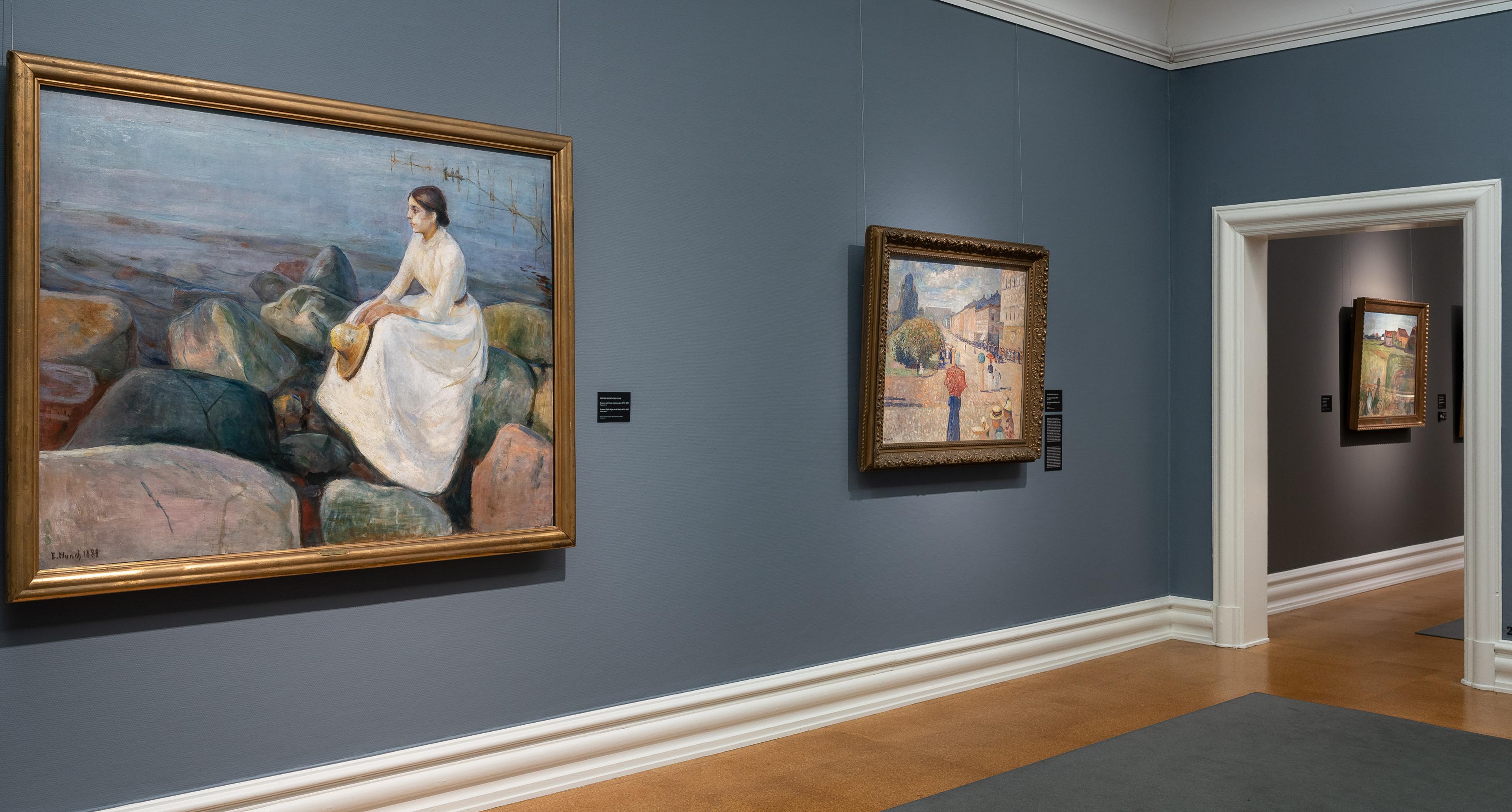Et utstillingsrom med blå vegger, og to malerier av Edvard Munch.